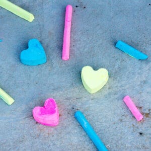 Colored heart-shaped and stick-shaped chalk pieces, including blue, pink, and yellow, scattered on a gray surface.